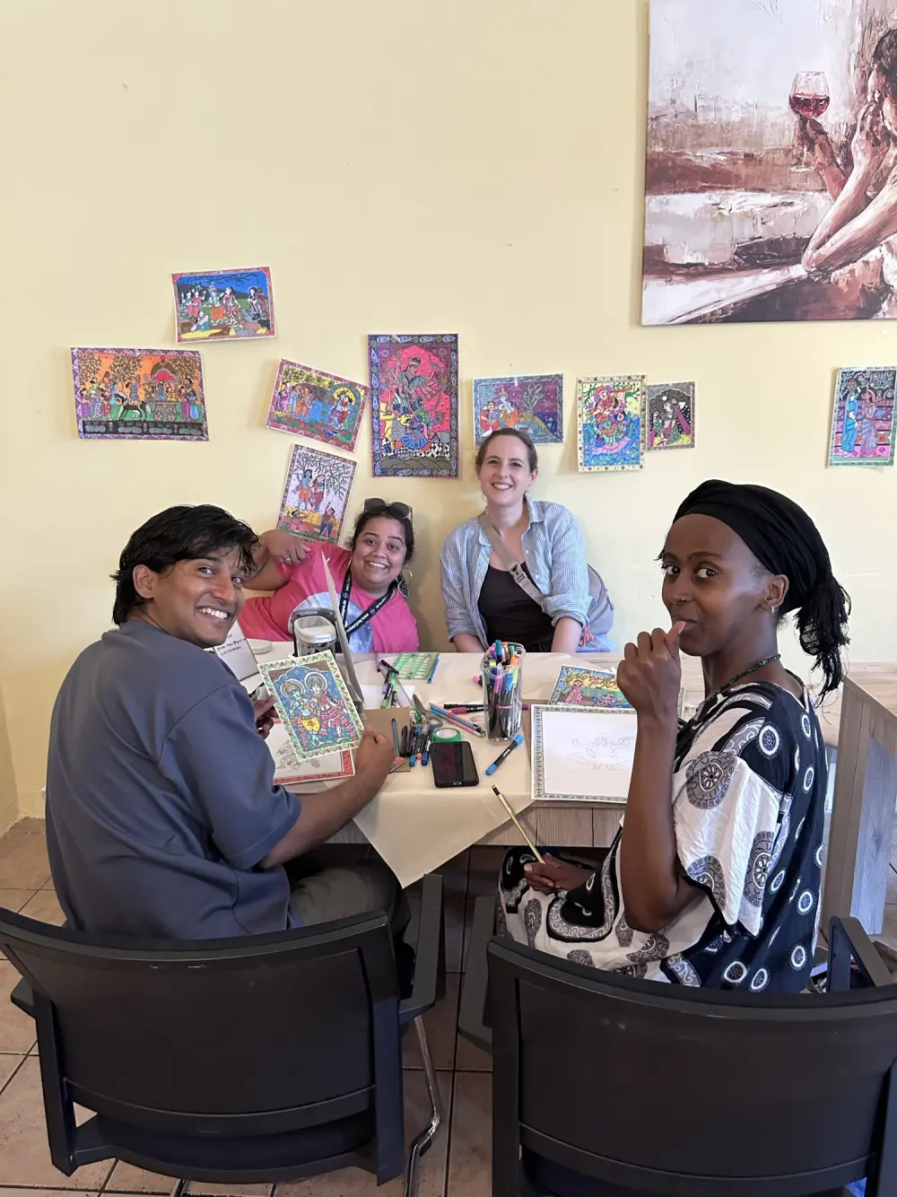 Priya and friends around a table covered in paint pens, colourful folk art on the wall behind them