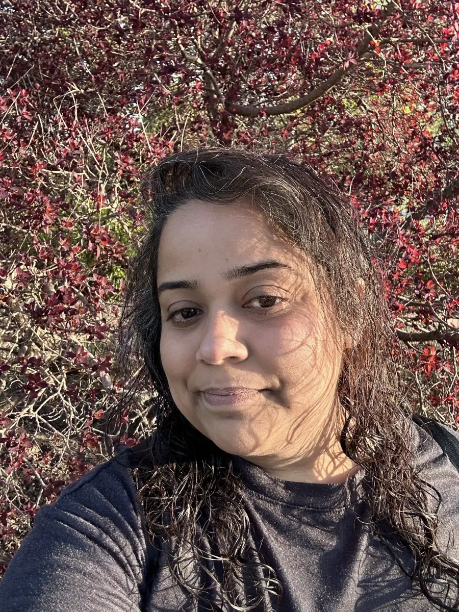 Priya smiling under a tree with deep red leaves