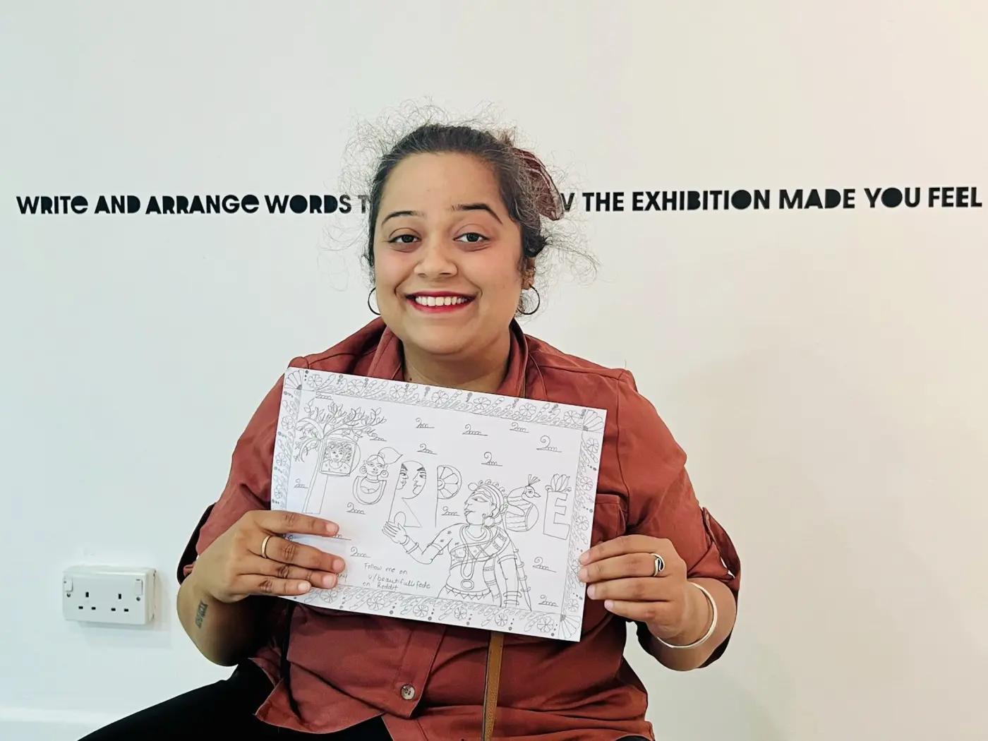 Priya at an exhibition, holding up a hand-drawn folk art piece